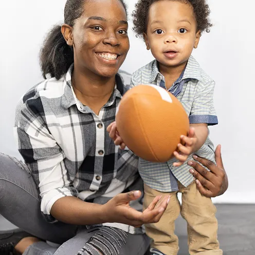 Smiling woman holding toddler who is holding a football.