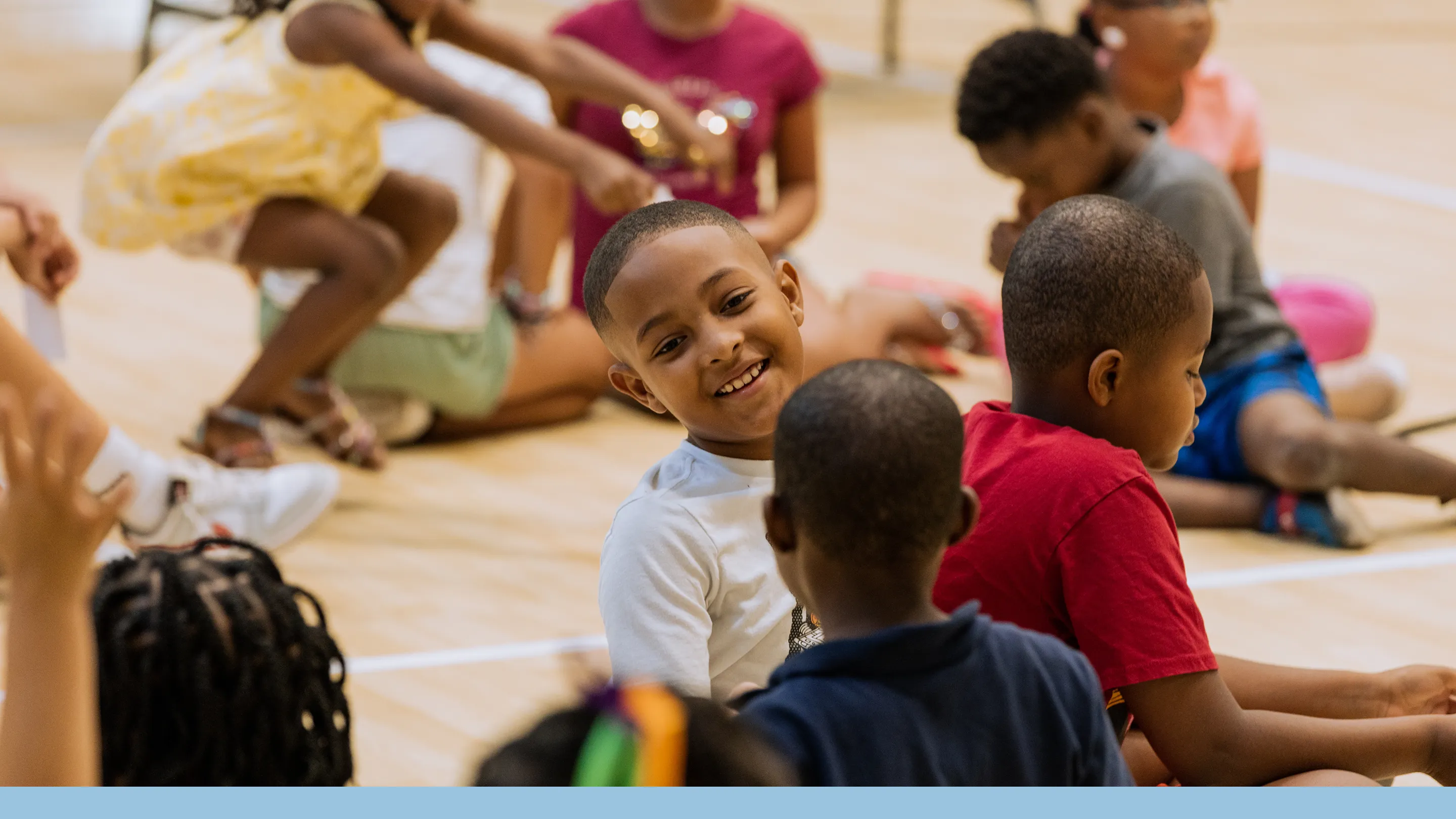 Group of children sitting and interacting on a gym floor during an indoor activity.