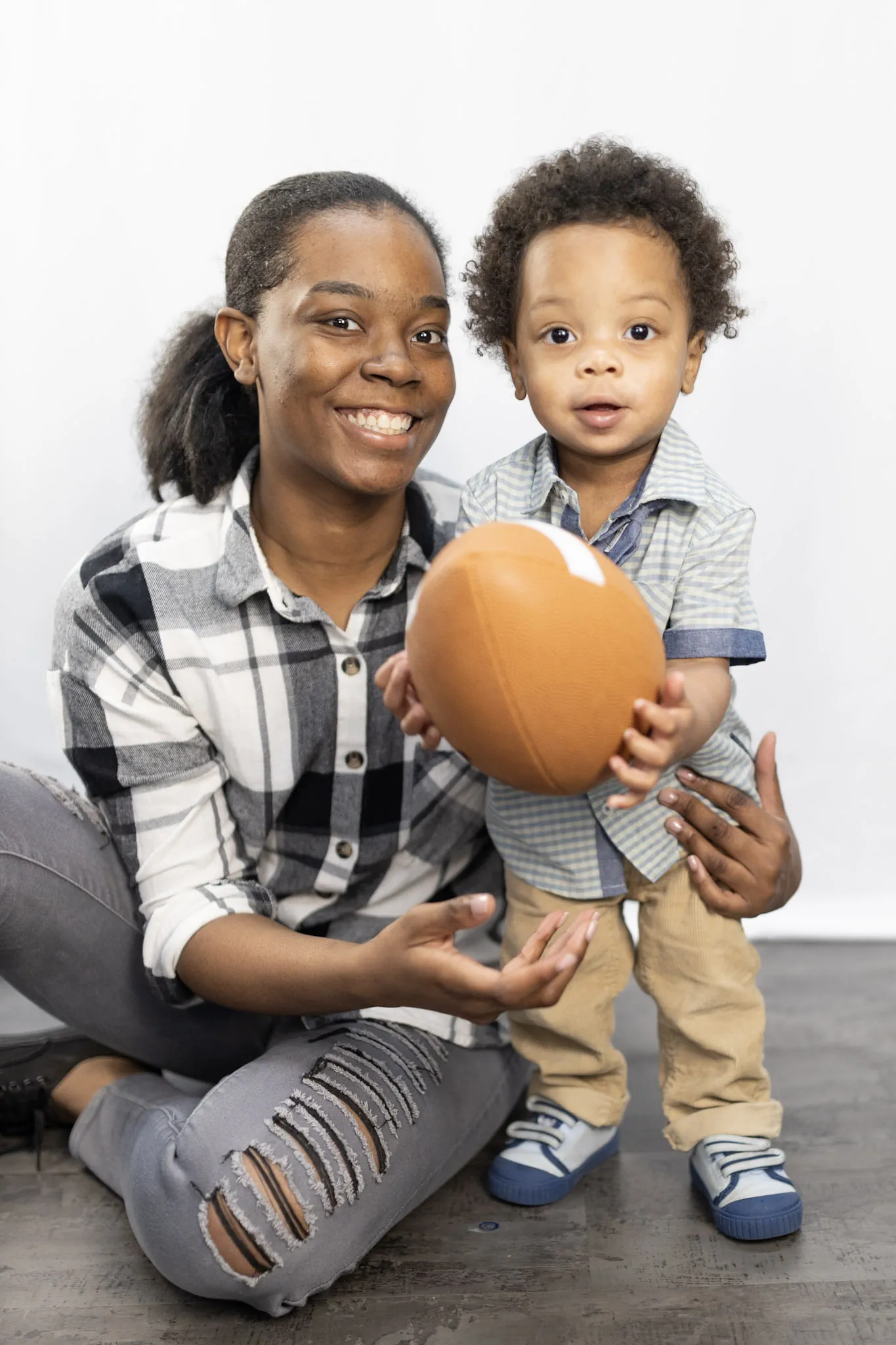 Smiling woman holding toddler who is holding a football.
