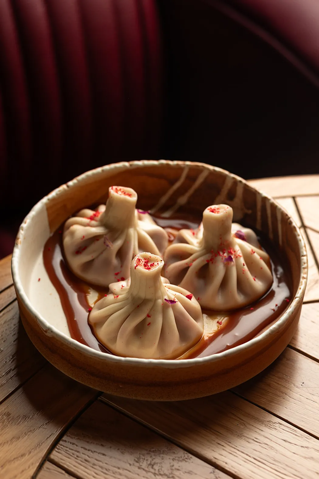 Three dumplings served in a round bowl with sauce, garnished with red seasoning.