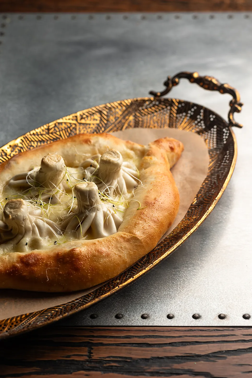 Georgian khachapuri bread with four dumplings on top in an ornate golden tray.