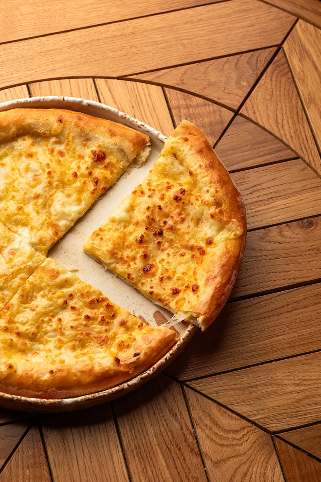Cheese pizza with a slice being pulled away on a ceramic plate on a wooden table.