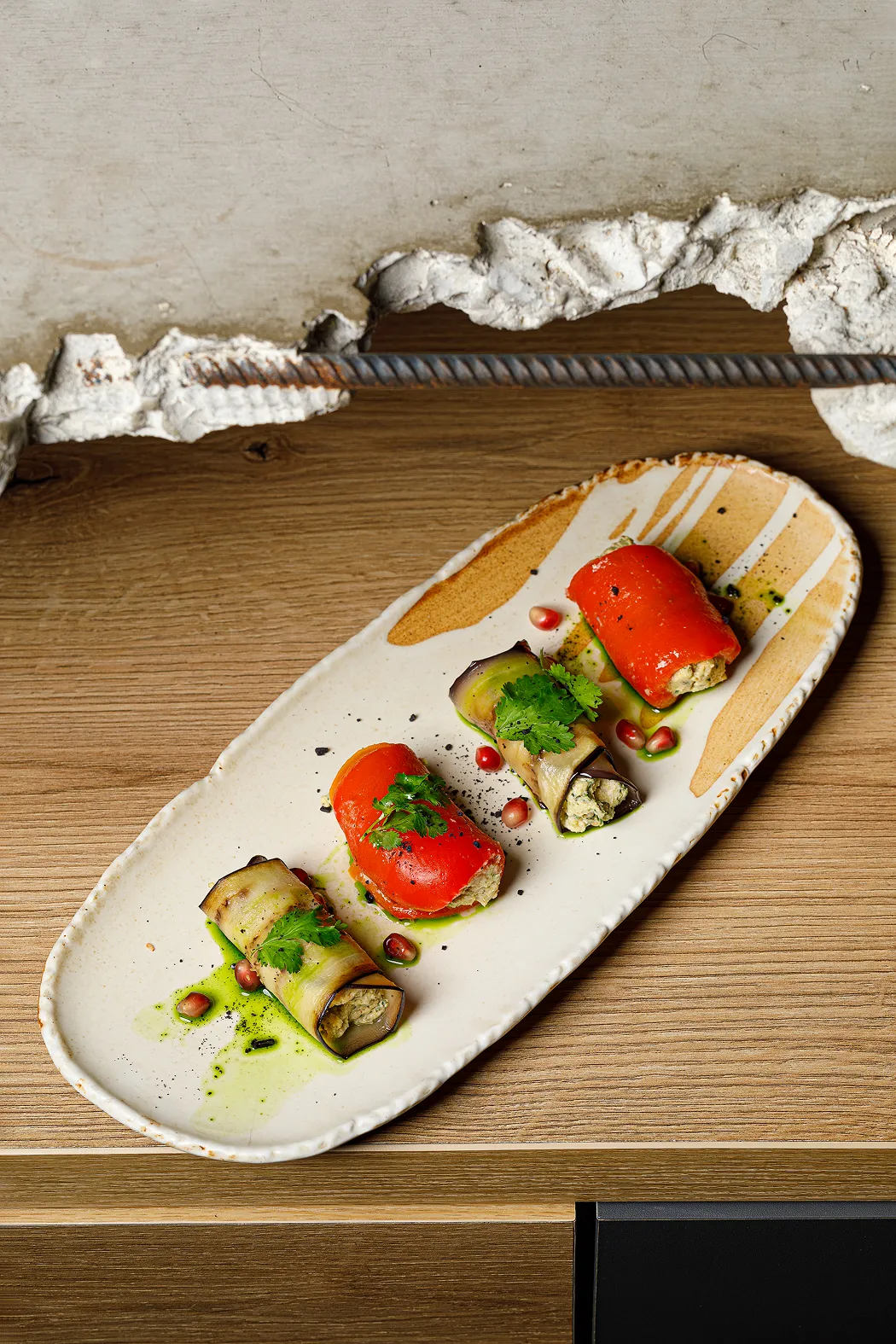 Four gourmet vegetable rolls with green garnish and pomegranate seeds on an elongated ceramic plate.