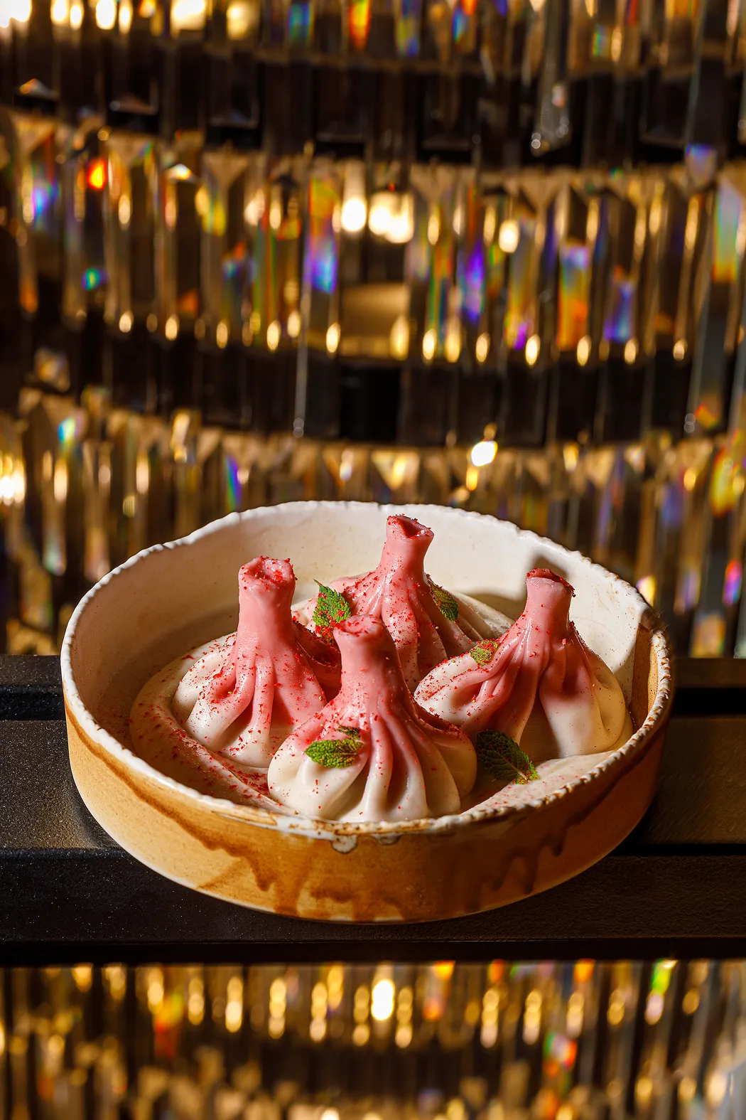 Four pink and white dumplings garnished with green mint leaves in a beige ceramic bowl with a decorative background.
