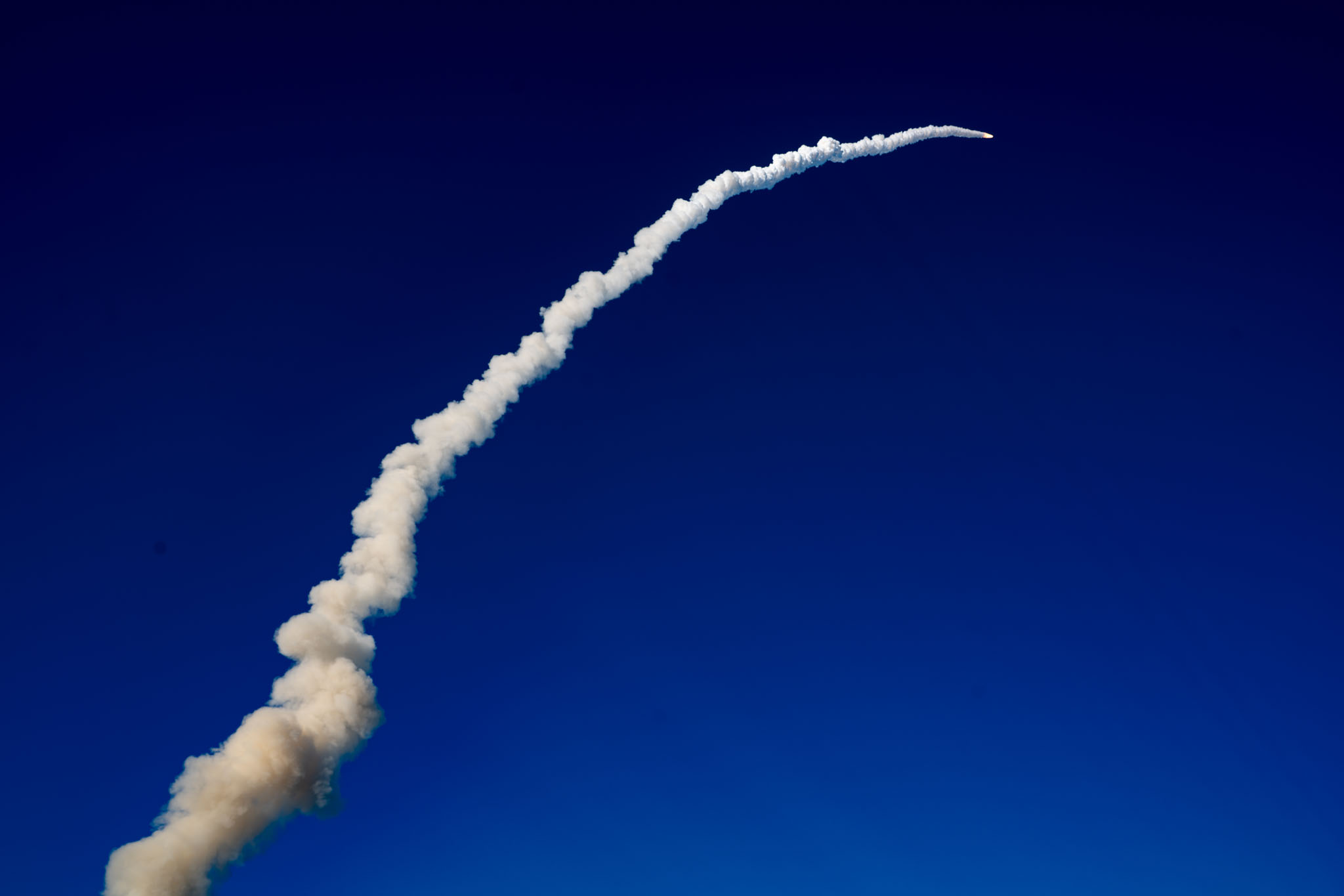 Artemis 2 rocket arcing across a clear blue sky with a smoke trail