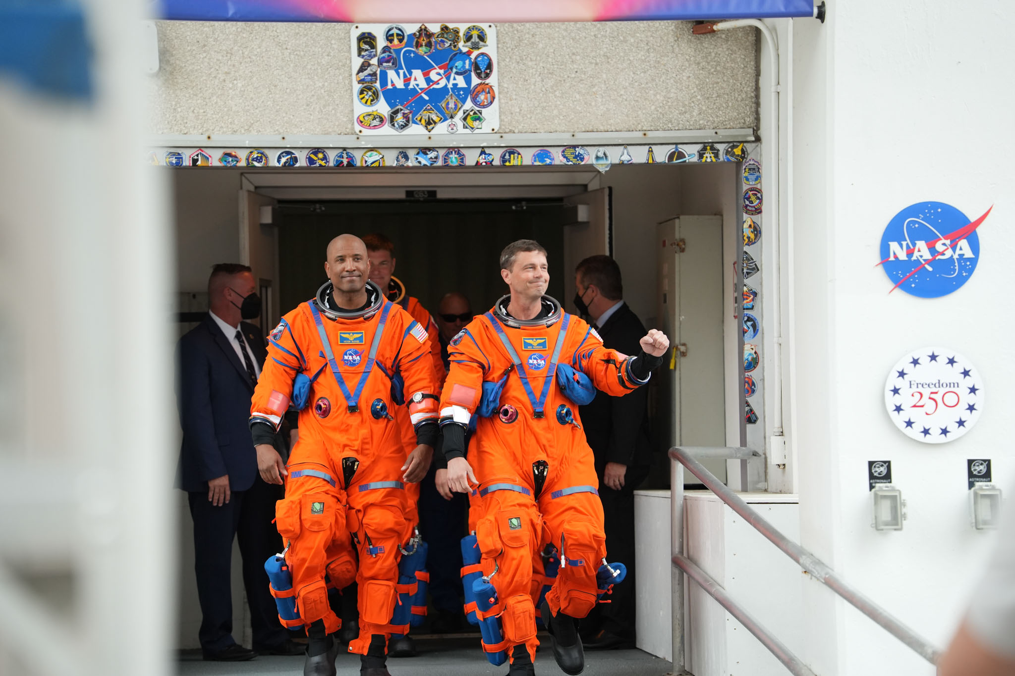 Artemis 2 crew members in orange launch-and-entry suits walking out of a NASA facility