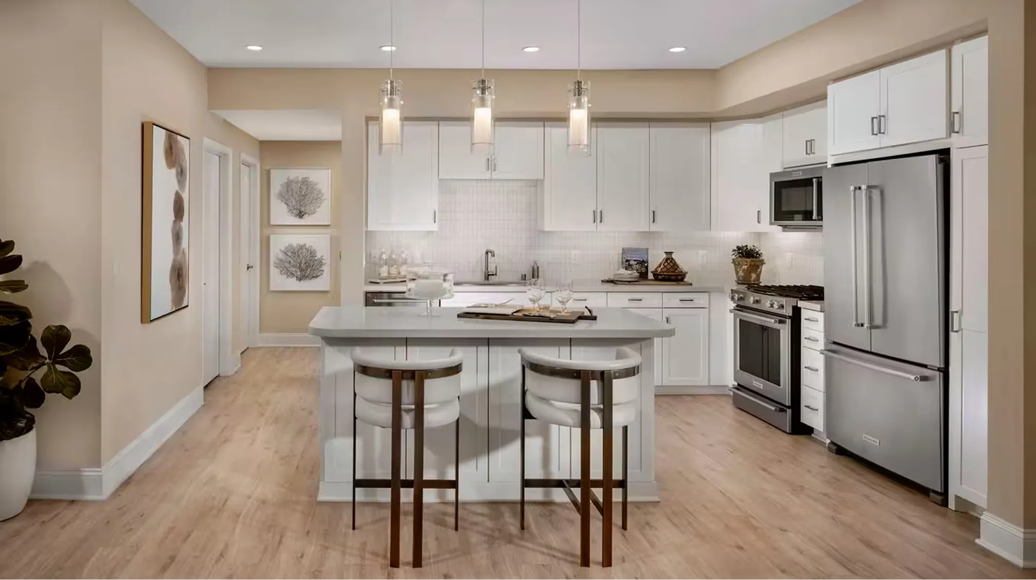 Modern kitchen with white cabinetry, stainless steel appliances, island with two stools, and pendant lighting.