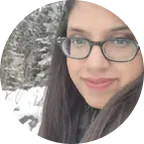 Woman with glasses smiling outdoors in a snowy forest setting.
