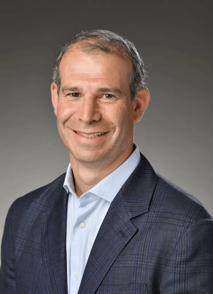 Headshot of Dr. Jeffrey Geller MD, a smiling man with short gray hair, wearing a blue checkered blazer and light blue shirt, against a gray background, conveying a professional tone.