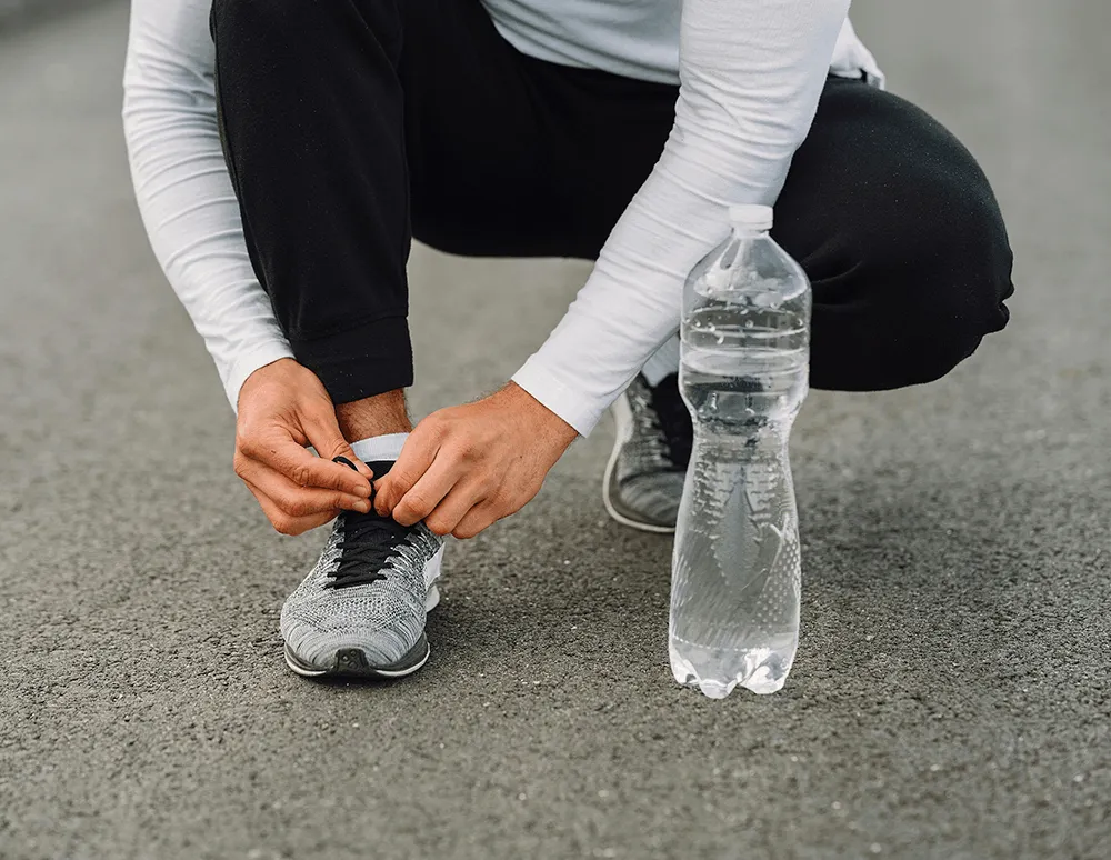 A person in athletic wear crouching down to tie their sneaker outdoors, illustrating the improved mobility and active lifestyle patients can achieve following total or partial knee replacement surgery.