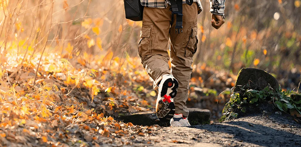 A person wearing hiking boots and pants walking through fallen autumn leaves, illustrating the return to an active lifestyle following successful revision hip surgery.