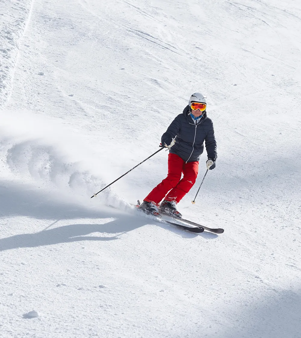 A skier in a red jacket and black pants skiing downhill on a snow-covered slope, illustrating the active lifestyle patients can return to following minimally invasive hip replacement surgery.
