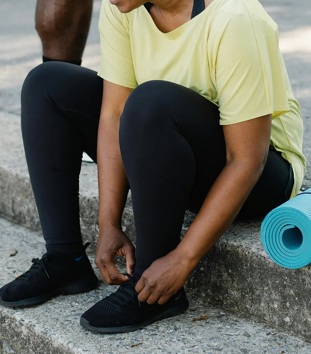 A person in athletic wear kneeling on one knee outdoors while placing a yoga mat on the ground, illustrating the flexibility and active lifestyle patients can return to after robotic knee replacement surgery.