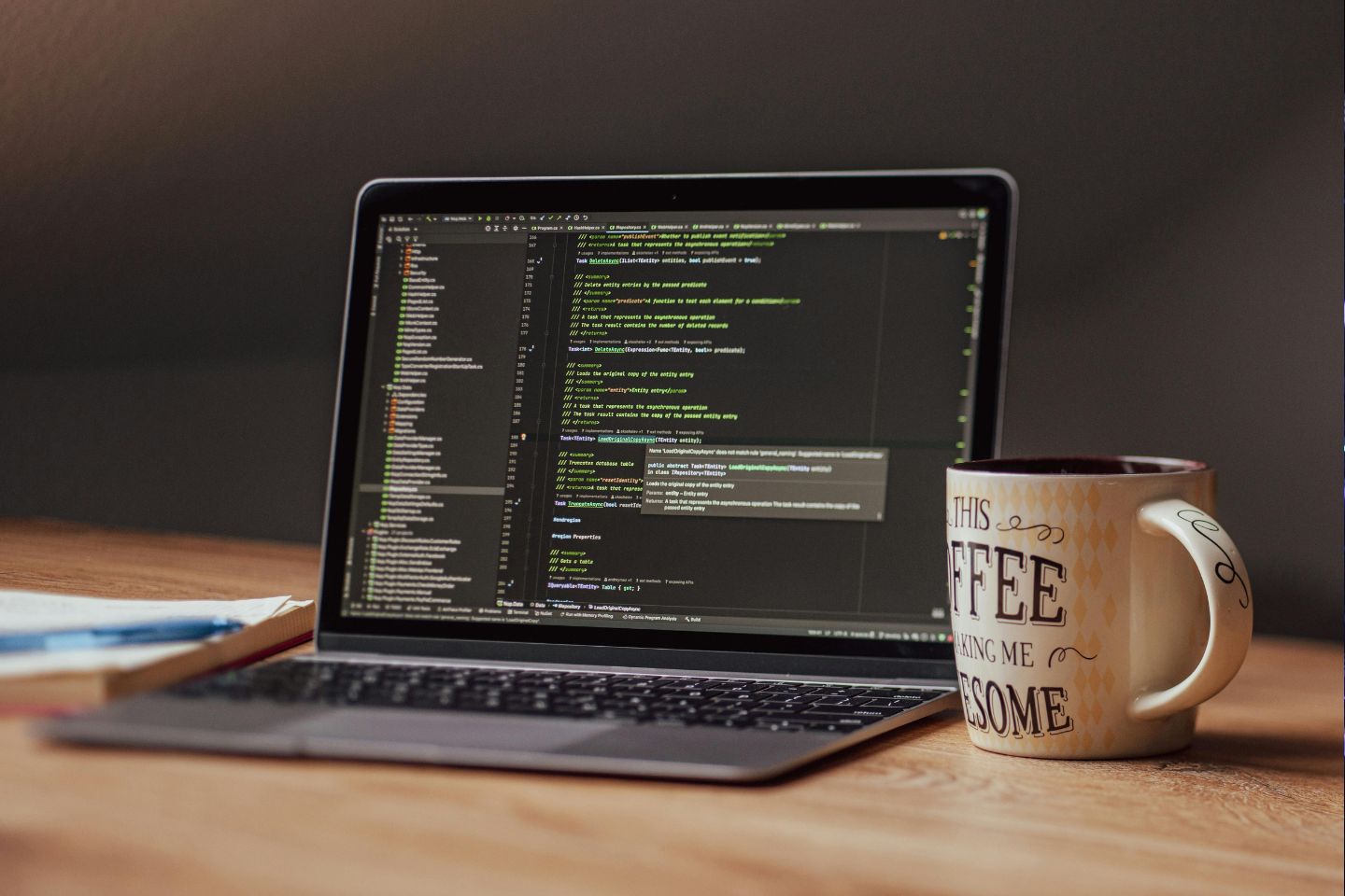 Open laptop on wooden desk displaying a programming code editor, with a coffee mug that says 'This coffee is making me awesome' beside it.
