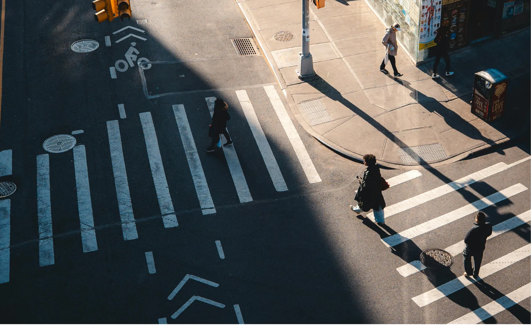 Aerial view of five people walking across a city crosswalk with sun casting long shadows.