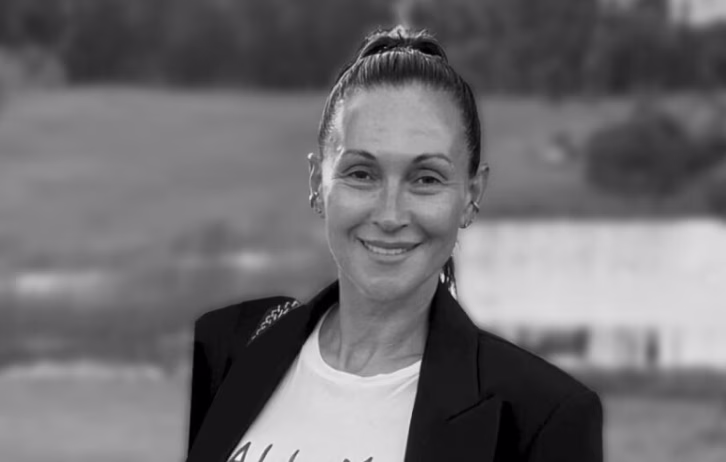 Woman with tied-back hair wearing a blazer and smiling in an outdoor setting.