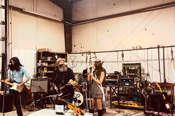 Four-member band playing a show in a warehouse with guitars, drums, and sound equipment.