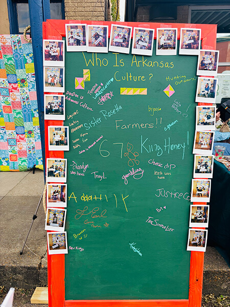 Green chalkboard with orange frame titled 'Who Is Arkansas Culture?' surrounded by Polaroid photos, containing colorful handwritten names and words related to Arkansas culture and people.