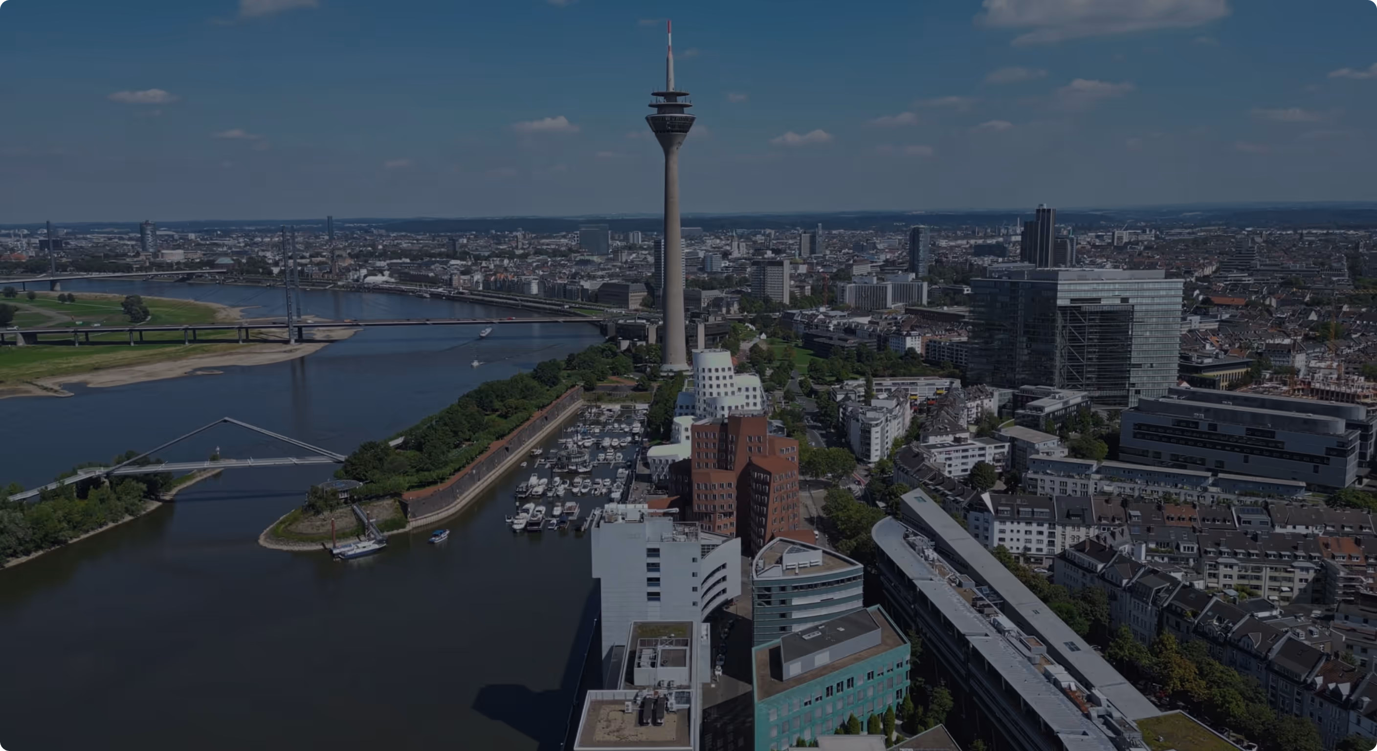 Luftaufnahme der Düsseldorfer Skyline mit Rheinturm und Rhein bei klarem Himmel.