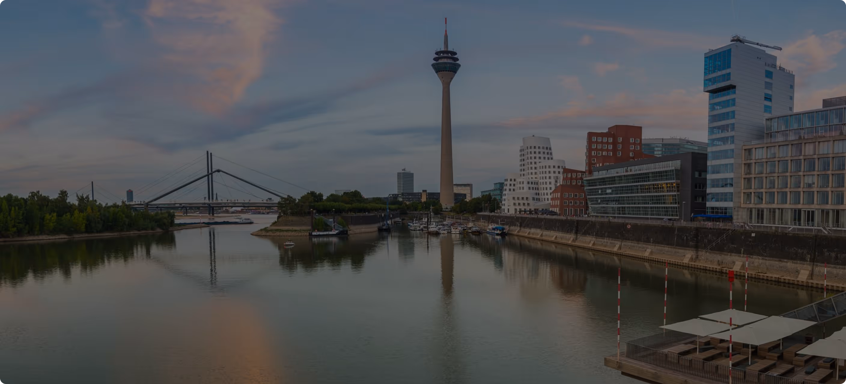 Panorama des Medienhafens in Düsseldorf mit Rheinturm und moderner Architektur am Wasser bei Abenddämmerung.