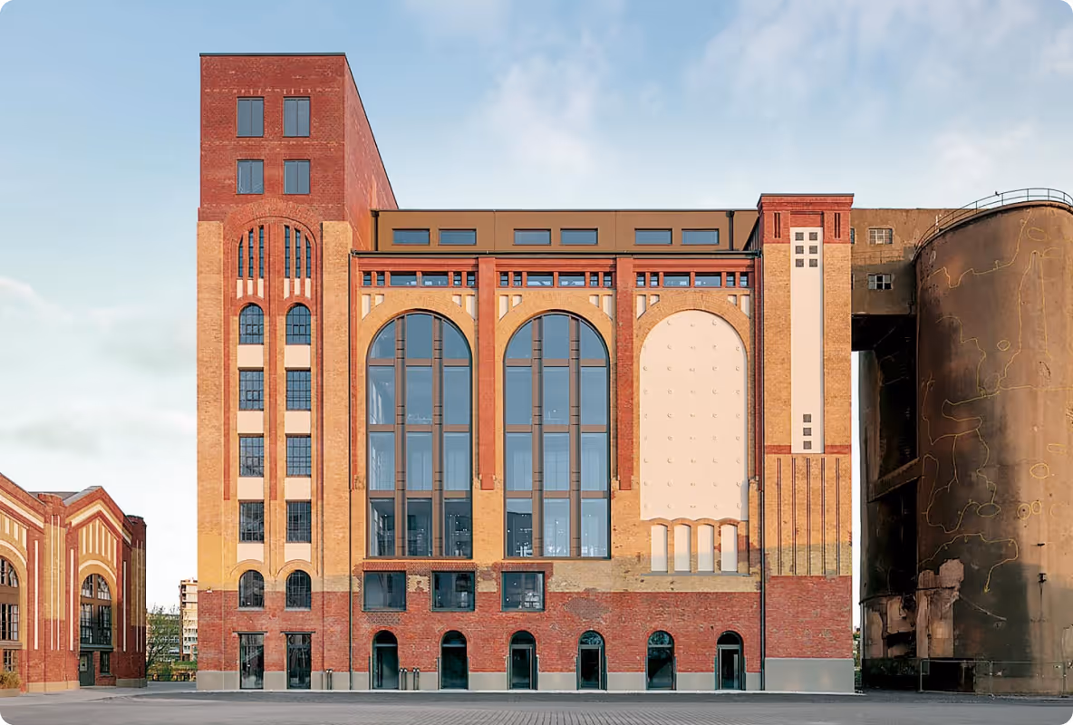 Neues renoviertes Industriegebäude mit großen, hohen Fensterbögen und sichtbar rotem Backstein.