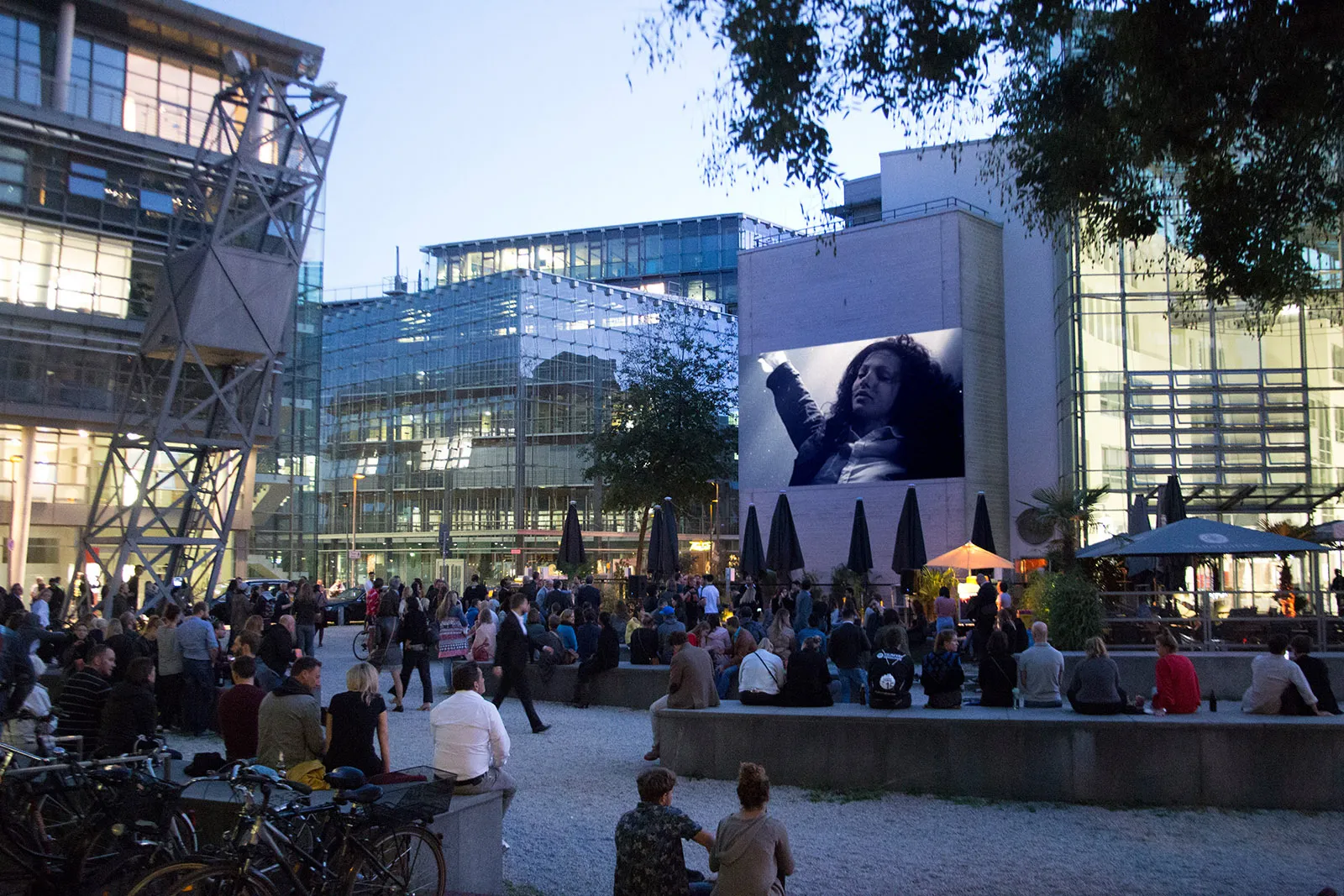 Menschen schauen einen Film, der auf einem Gebäudewandprojektor in einem Innenhof gezeigt wird.