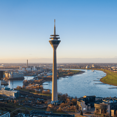 Der Rheinturm-Turm neben dem Rhein in Düsseldorf bei klarem Himmel und Sonnenlicht.