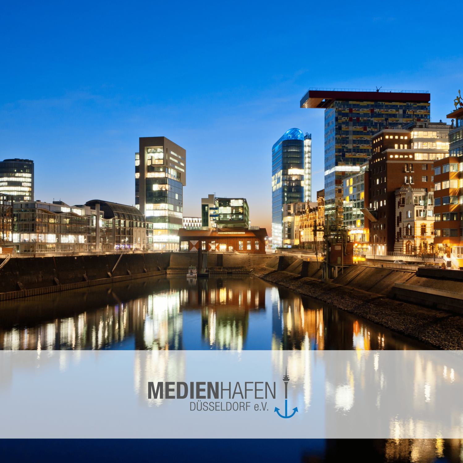 Abendliche Ansicht des Medienhafens Düsseldorf mit beleuchteten modernen Gebäuden und Wasserspiegelungen.