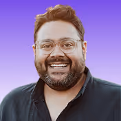 Smiling man with glasses, beard, and dark shirt against a purple gradient background.