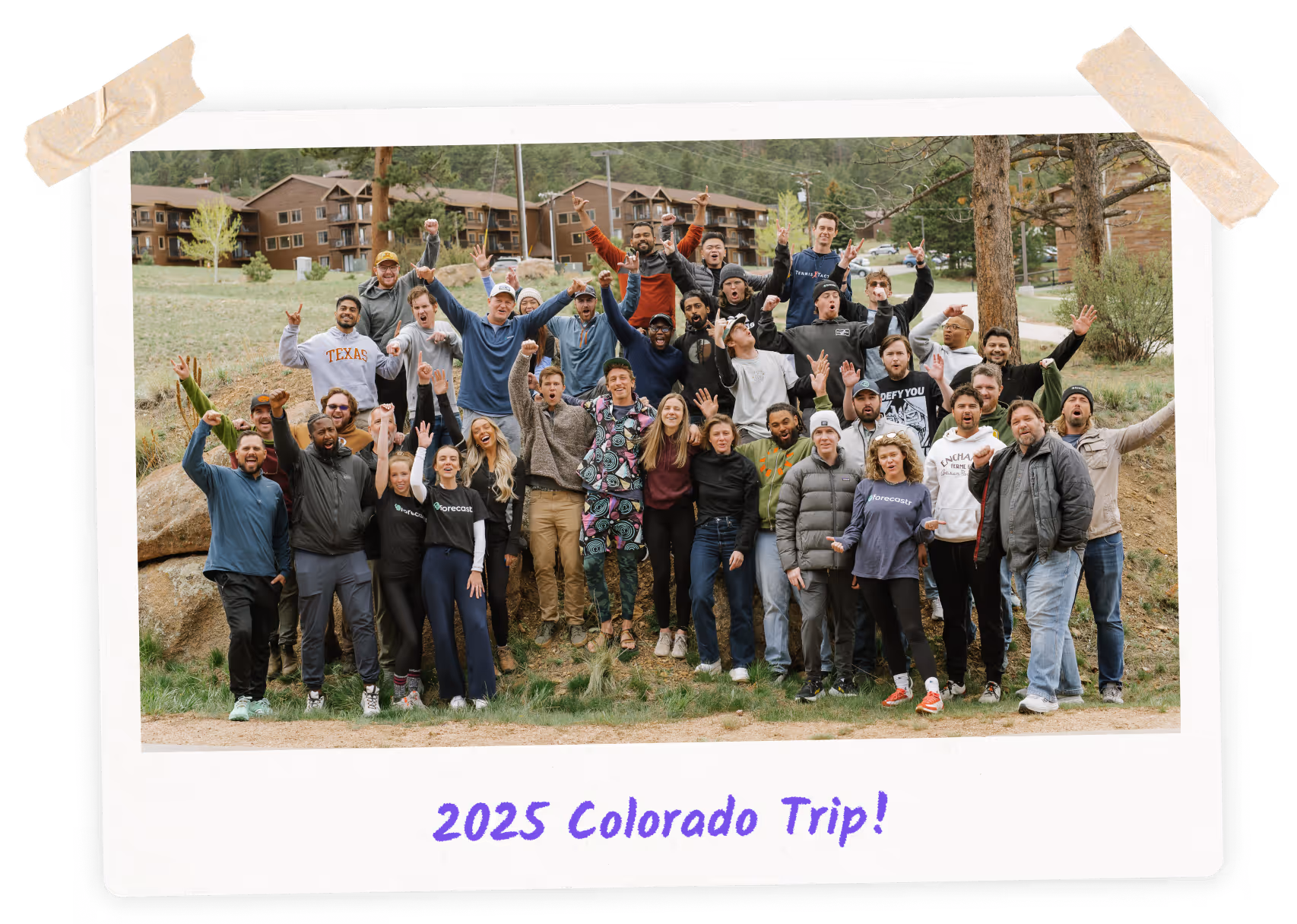 Large group of people outdoors in front of buildings, cheering and posing for a group photo.