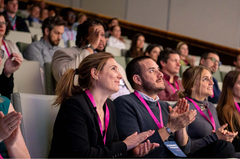 Audience members wearing lanyards sitting and applauding during an event or conference.