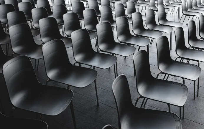 Rows of empty black chairs arranged in a large indoor space with tiled flooring.