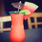 Red frozen cocktail in a tall glass garnished with a slice of watermelon, a lime wedge, and a small paper umbrella.
