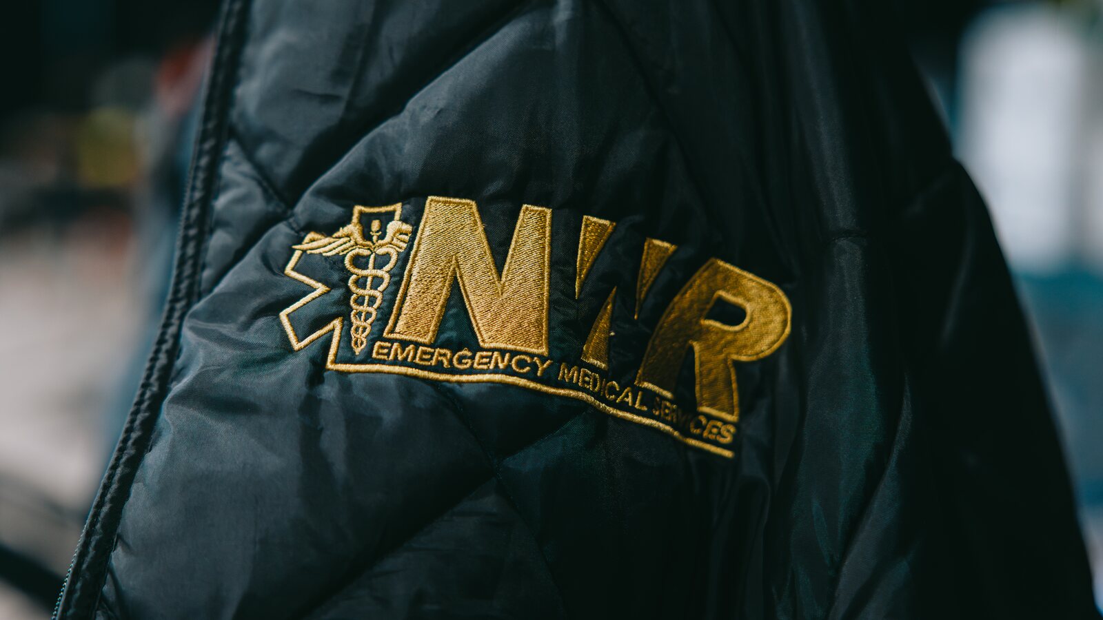 Gold-embroidered Northwest Rescue Emergency Medical Services crest stitched onto a crew jacket, representing the team's mission and why they serve.