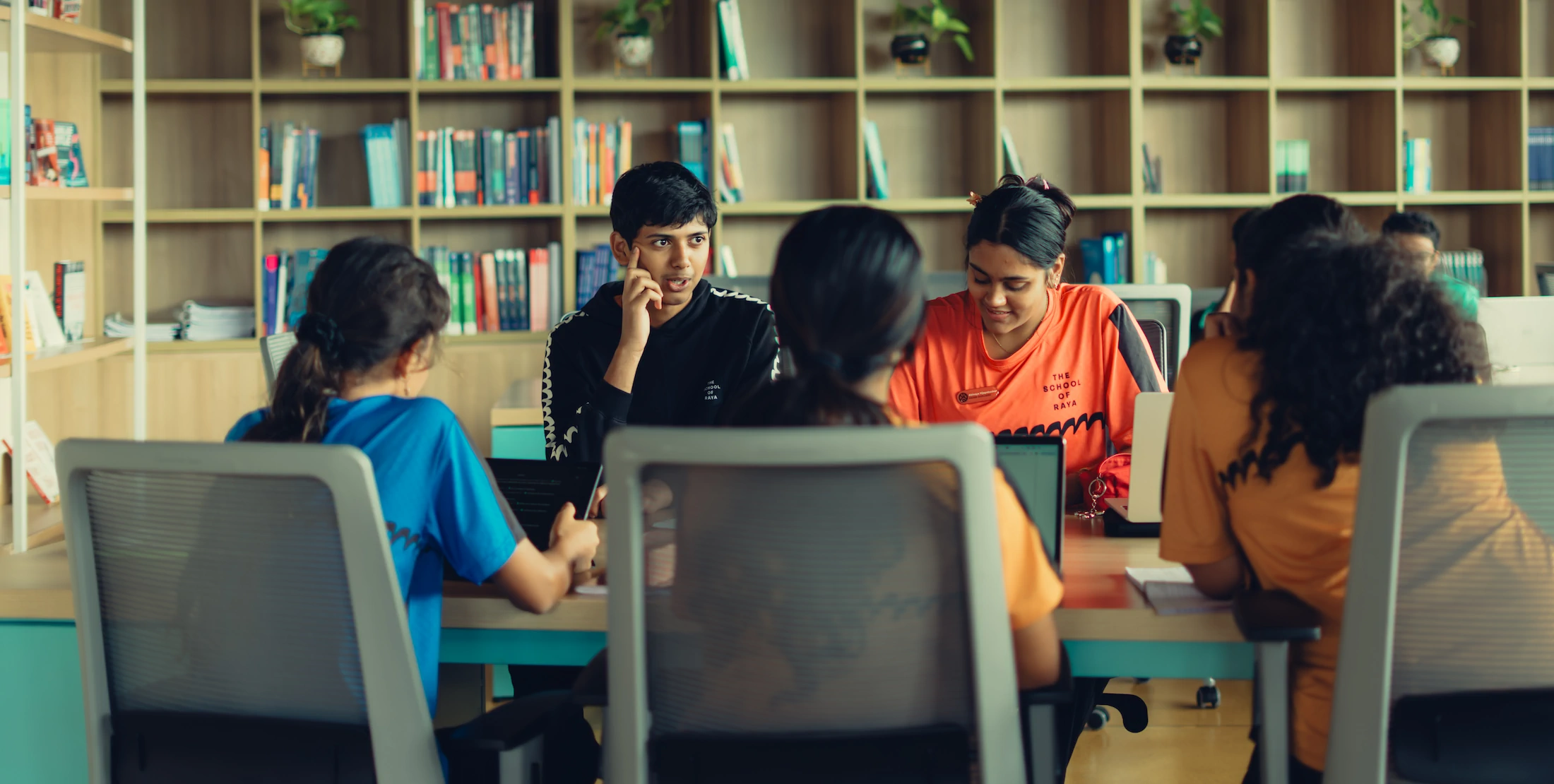 Students sitting around a table in a library, some using laptops and engaging in discussion.