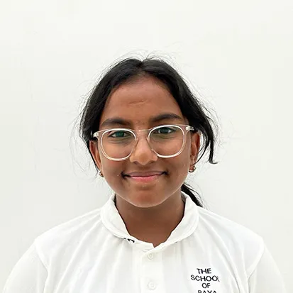 Smiling girl wearing clear glasses and a white shirt with a school logo on a white background.