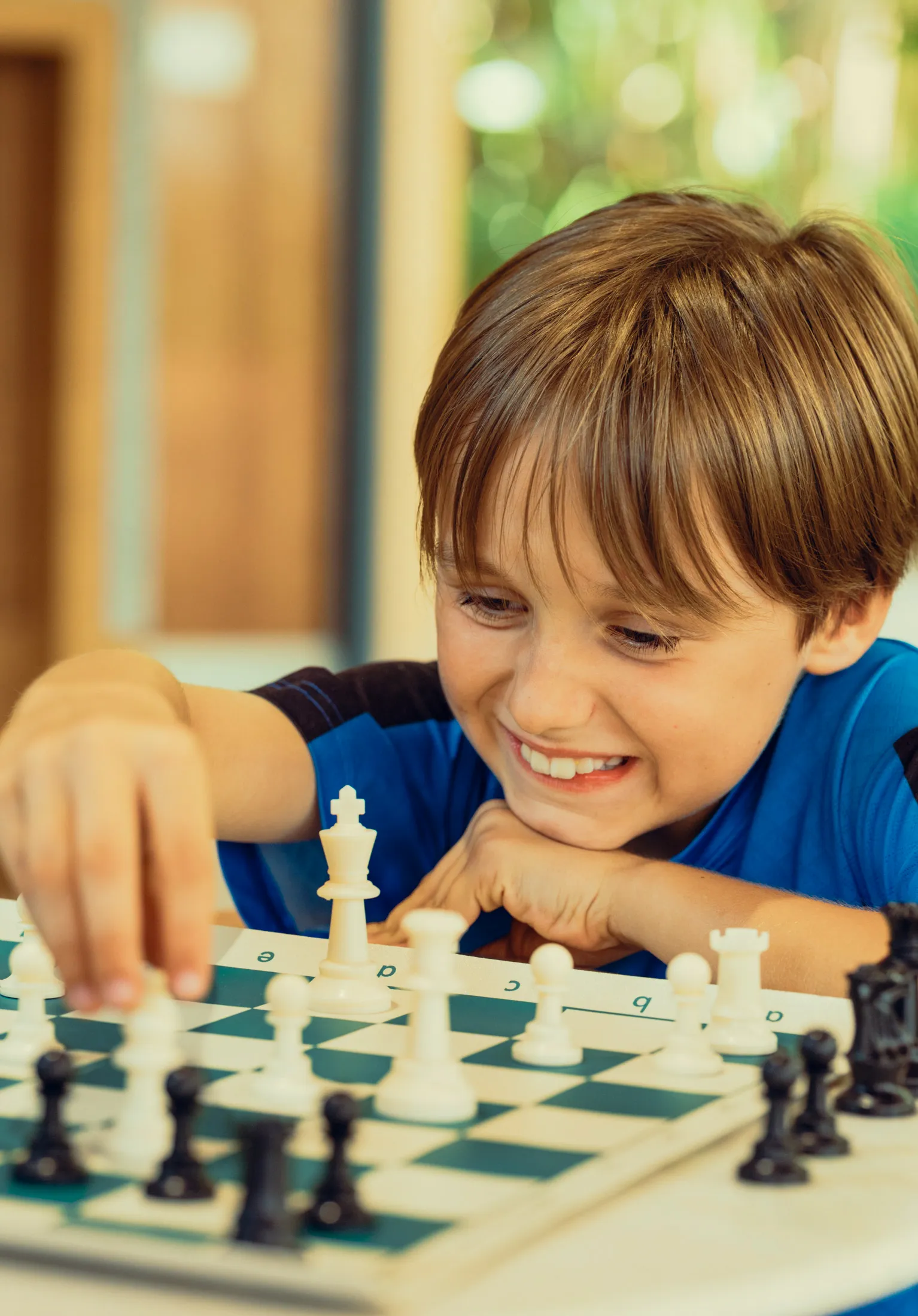 Young boy smiling and reaching to move a white chess piece on a chessboard.