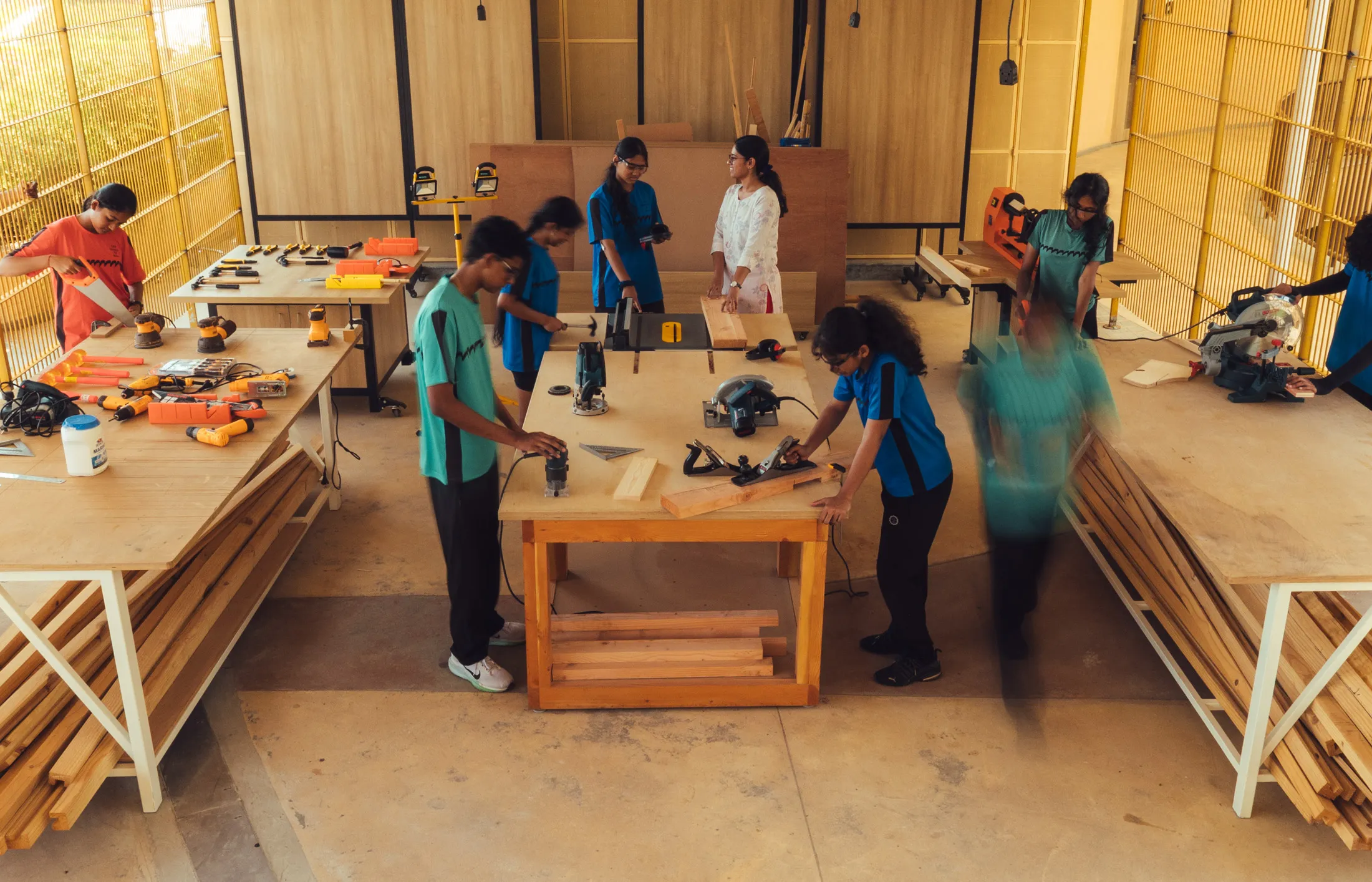 Students working with wood and tools in a woodworking workshop with yellow walls and shelves.