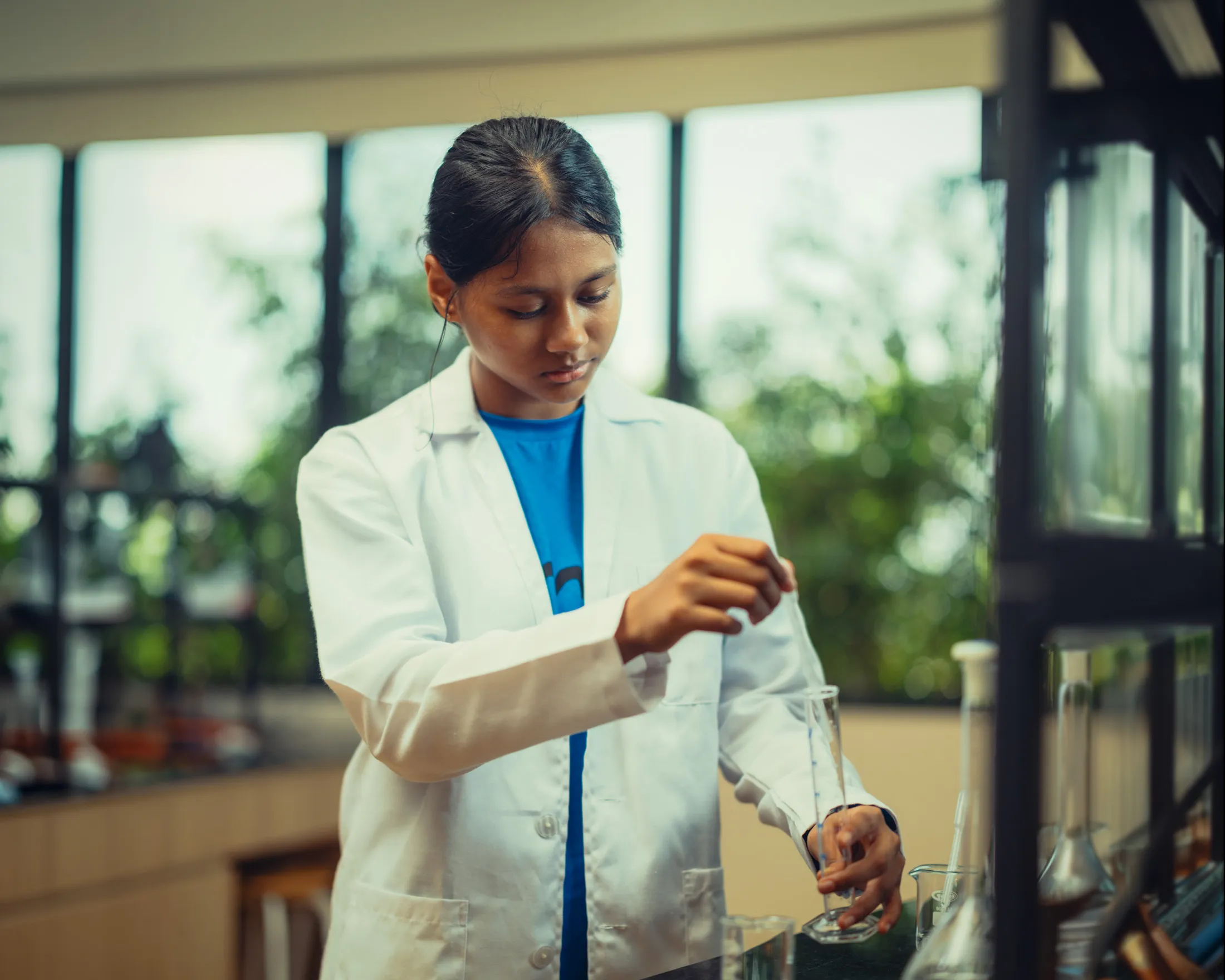 Young woman in a lab coat conducting an experiment with glassware in a bright laboratory.