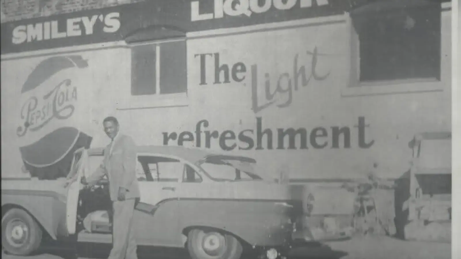 Historical photograph of a Black businessman beside a car in front of Smiley’s Liquor on Walnut Street, Helena, Arkansas