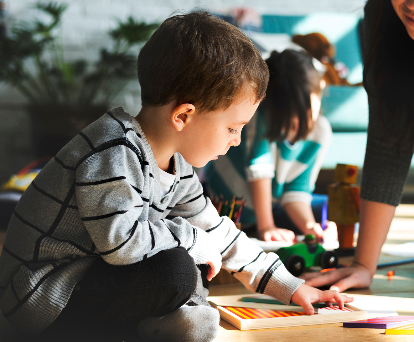 Two young children sitting at a colorful table, smiling and drawing in a bright playroom.