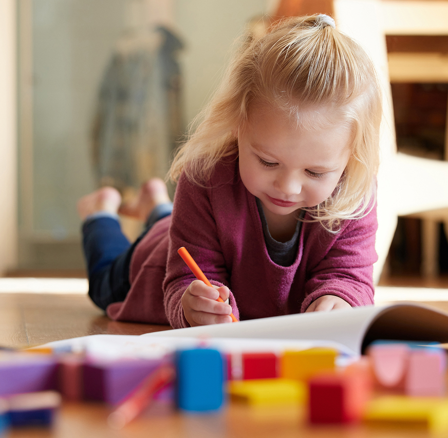 Yellow baby shirt with a green giraffe print placed beside wooden toys and folded white cloth on a light gray surface.