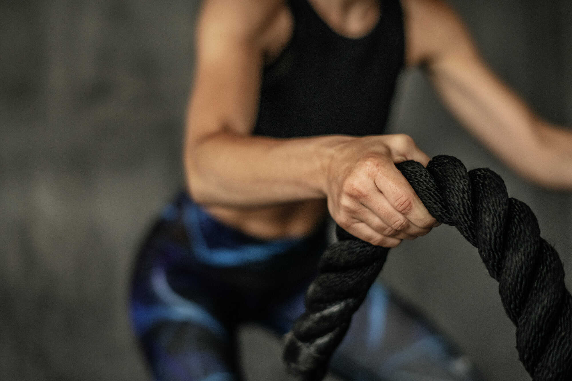 Close-up of a person gripping a thick black battle rope during an intense workout.