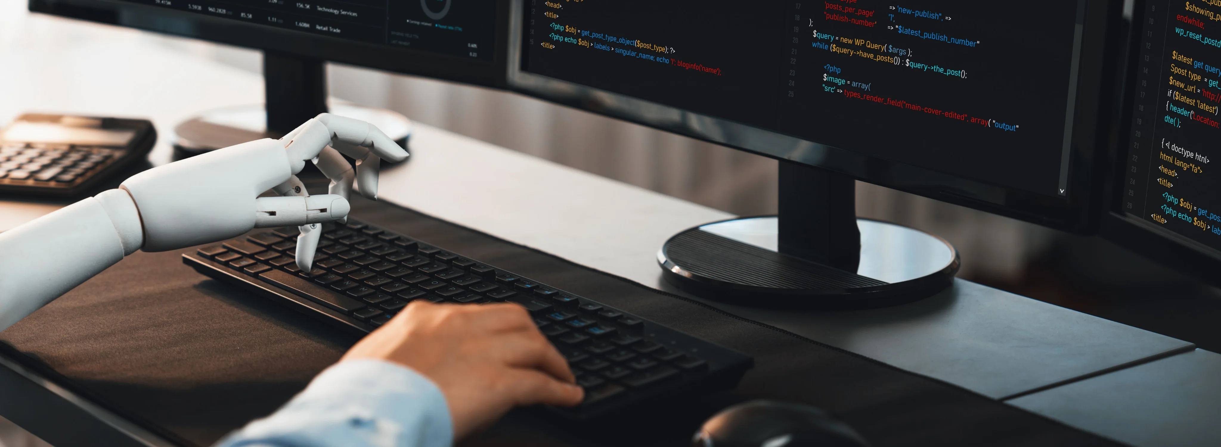 Human hand and robotic hand collaborating on typing at a computer keyboard with coding displayed on monitors.