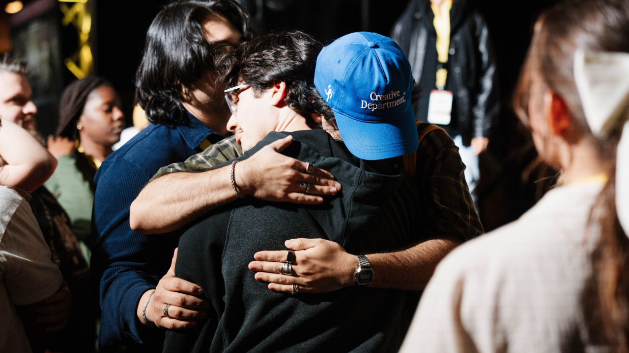 Three people embrace in a group hug among a crowd