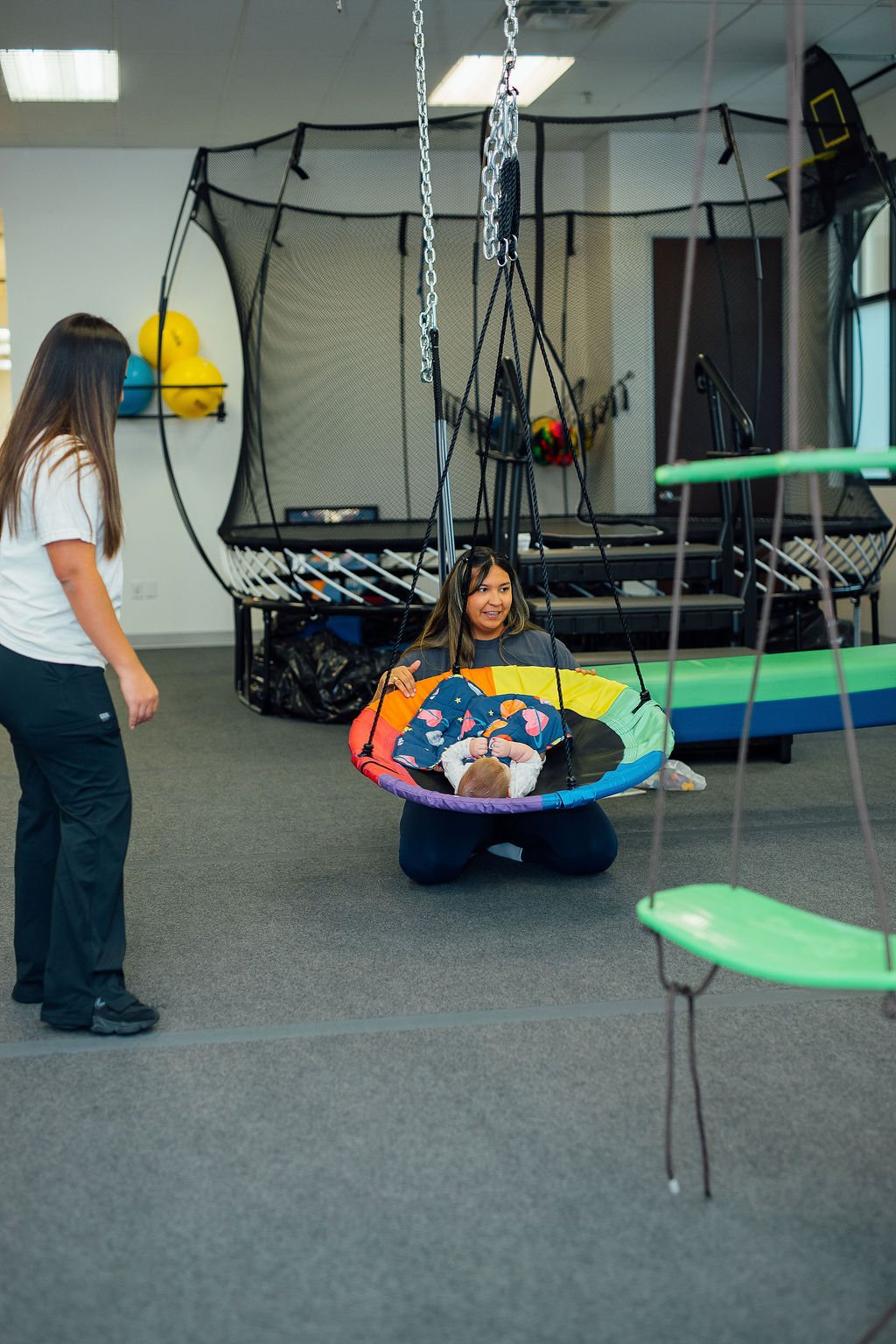 Child relaxing in a saucer swing with therapists nearby in the Oaklin Lane sensory gym