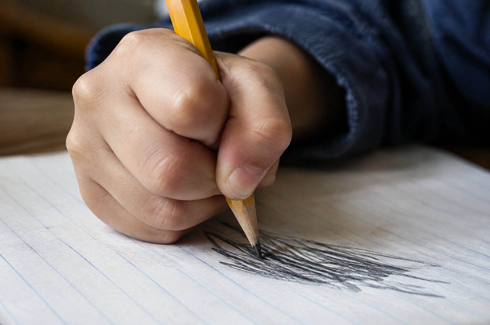 Child gripping a pencil tightly and pressing hard on lined paper