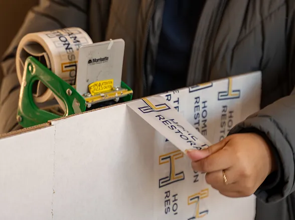 Home Team Restoration technician sealing a branded box during contents pack-out in Goldsboro, NC