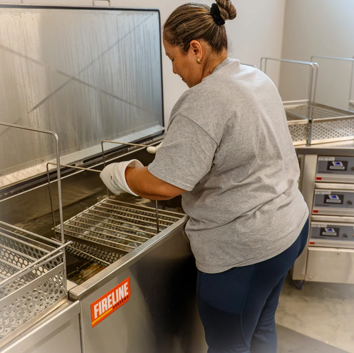 Person wearing a gray shirt placing a metal basket into an industrial stainless steel cleaning machine.