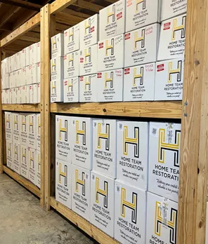 Wooden shelves filled with neatly stacked Home Team Restoration branded storage boxes.
